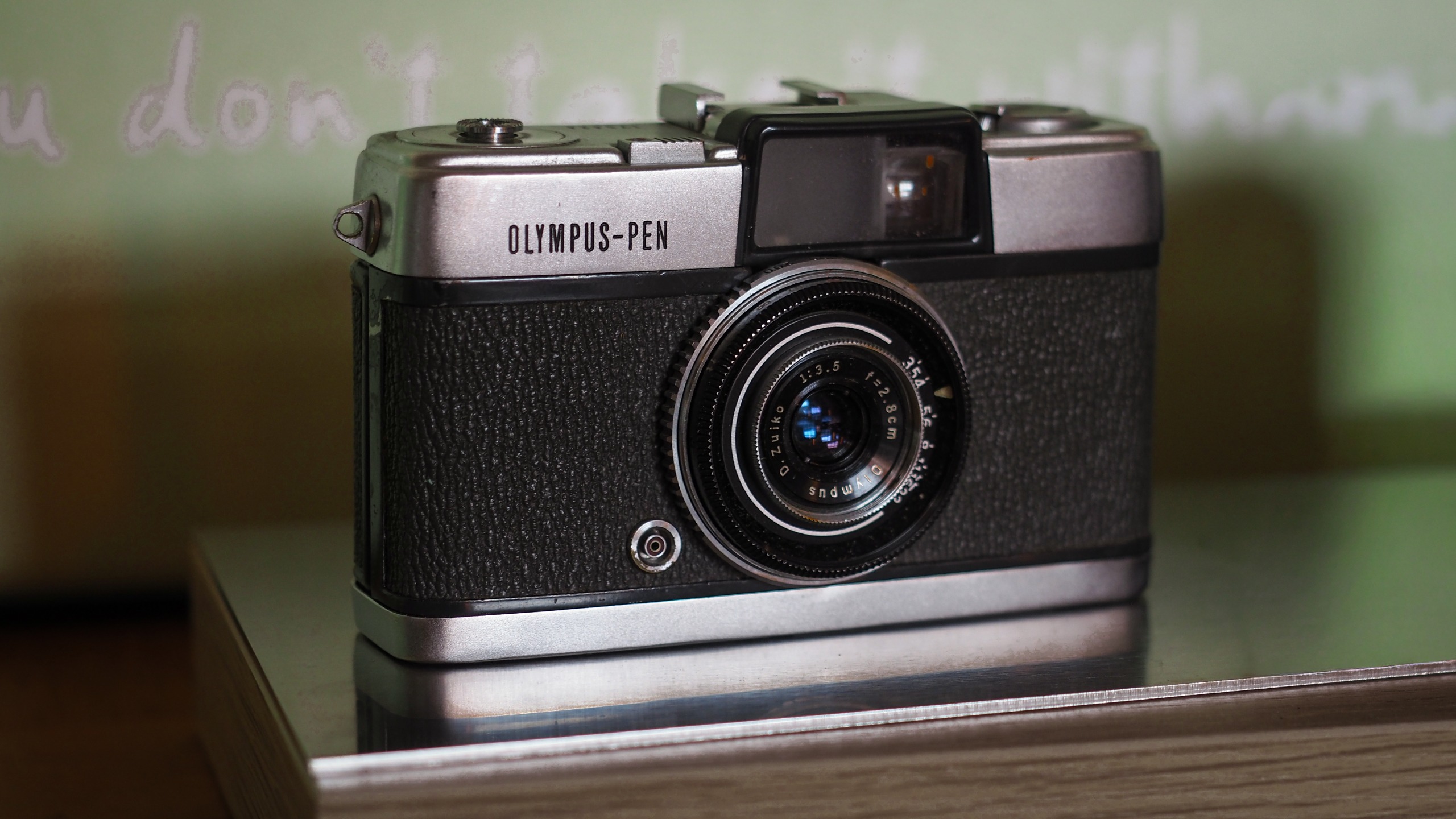Olympus PEN (1959) on a silver surface, in front of a green background