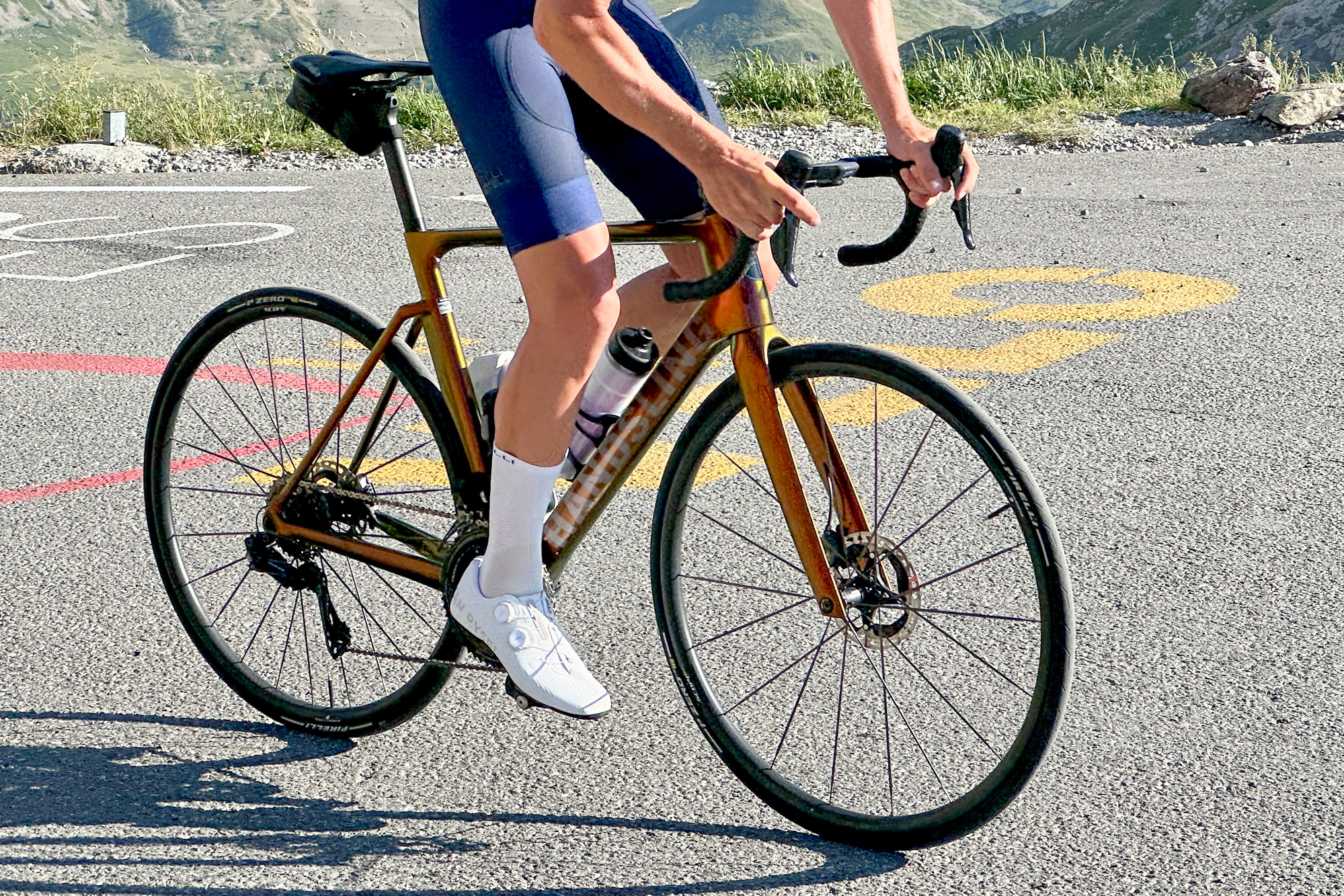 Lower half of a man riding an orange bike wearing blue shorts and white shorts