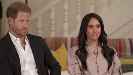 Prince Harry and Meghan Markle (Sussex) sit down for an interview in dress clothes. They are set up with a stairwell in the backdrop.