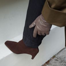 Woman wears black trousers, beige gloves, green trench coat and brown suede boots