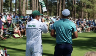 Brooks Koepka and his caddie seen from behind on a tee at The Masters