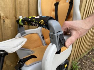 Topeak Babyseat II lab bar is shown in this image with a hand unclipping it from the Topeak Babyseat II