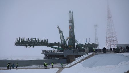 a greenish-gray and white rocket stands on its launch pad under an overcast sky