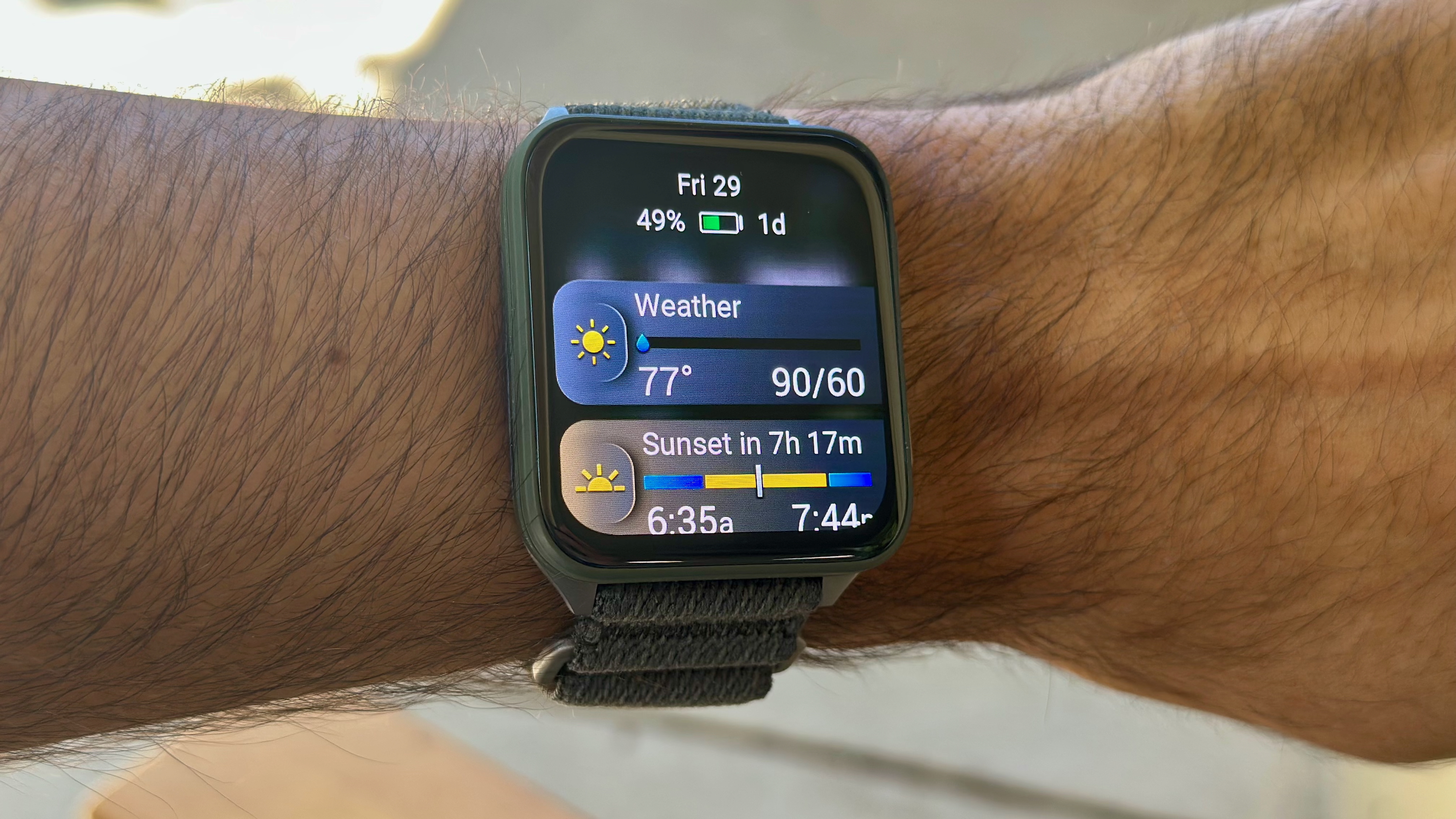 The Garmin Venu X1 on the author&#039;s wrist, showing the current battery percentage (49%) and time left (1 day) in AOD mode, along with glances for Weather and Sunset below.