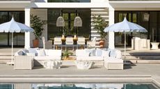 hamptons style outdoor patio area and poolside with large corner white rattan sofas and blue scalloped patio umbrellas