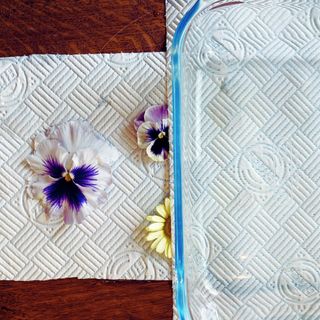 flowers on a piece of kitchen roll with another piece on top and a glass dish on top