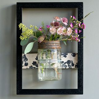 grey wall with black frame and glass jar with flower