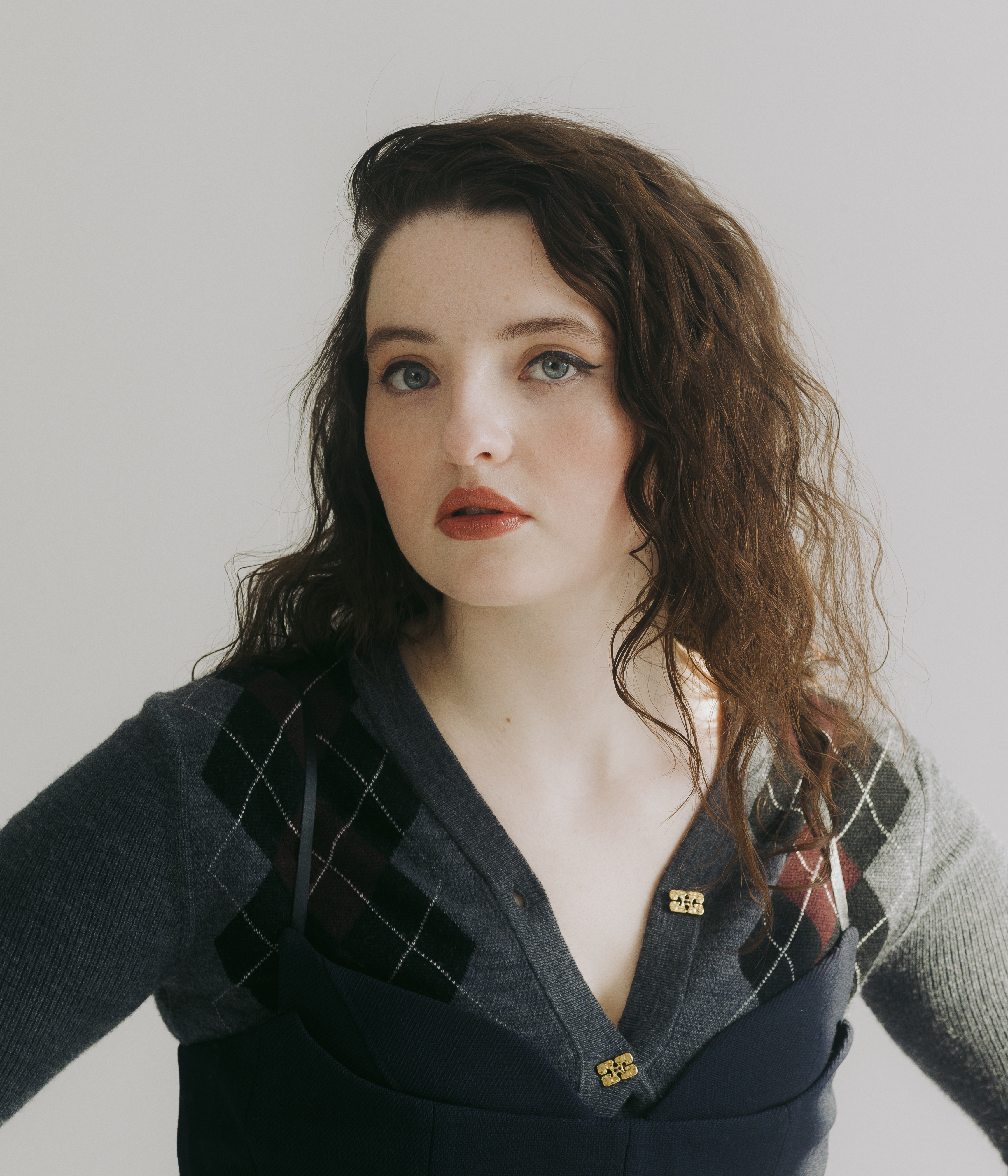 the testaments actress lucy halliday poses in a headshot wearing an argyle sweater with a black top over it