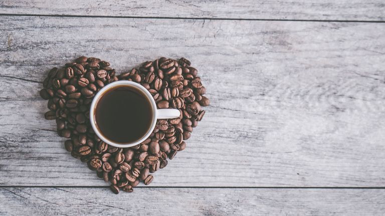 A cup of coffee surrounded by coffee beans in the shape of a heart