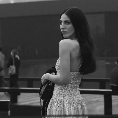 Writer Orion Carlotto stands on a bridge wearing a sequin floral dress on her way to the Chanel Metiers D'Art show