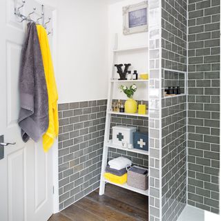 bathroom with white and grey tiles wall white door white ladder shelf and grey and yellow towel on hanger