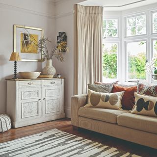 A living room with a beige sofa and mismatched patterned cushions on top