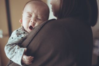 baby yawning on shoulder of woman