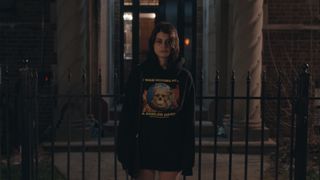 Sofia Black-D'Elia as mackenzie wearing a black sweatshirt standing outside of a building looking glum in a still from i love you forever