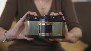 A person holds a vintage-style Widelux panoramic camera with a black body and brass-colored accents.