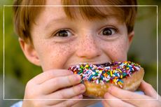 close up of happy child eating a doughnut covered in chocolate and sprinkles