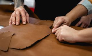 A man's hand cutting brown leather