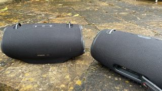 JBL Xtreme 4 and Xtreme 3 next to each other outside on the ground from behind