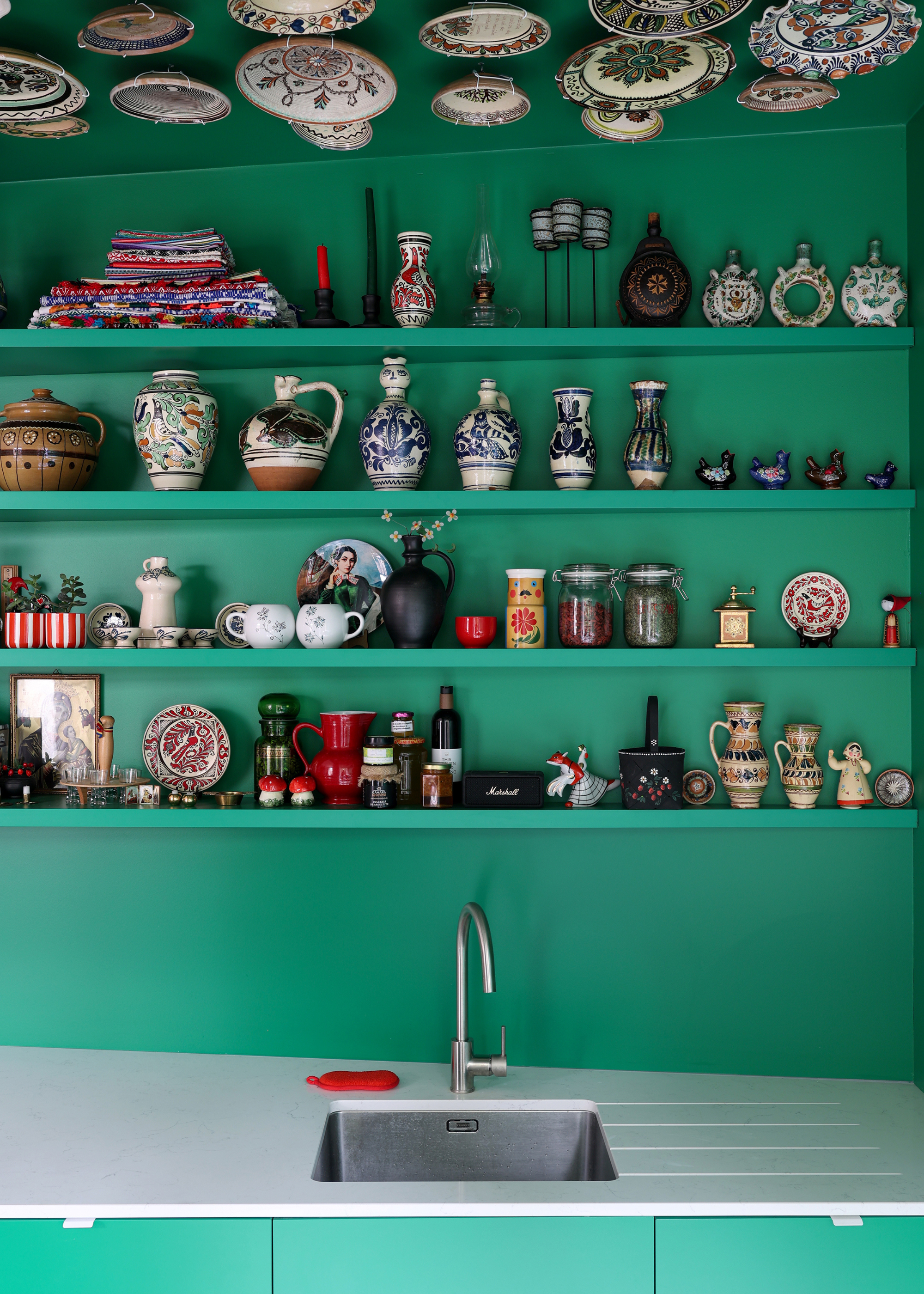 close up of a green kitchen with open shelving covered in pottery and nick nacks