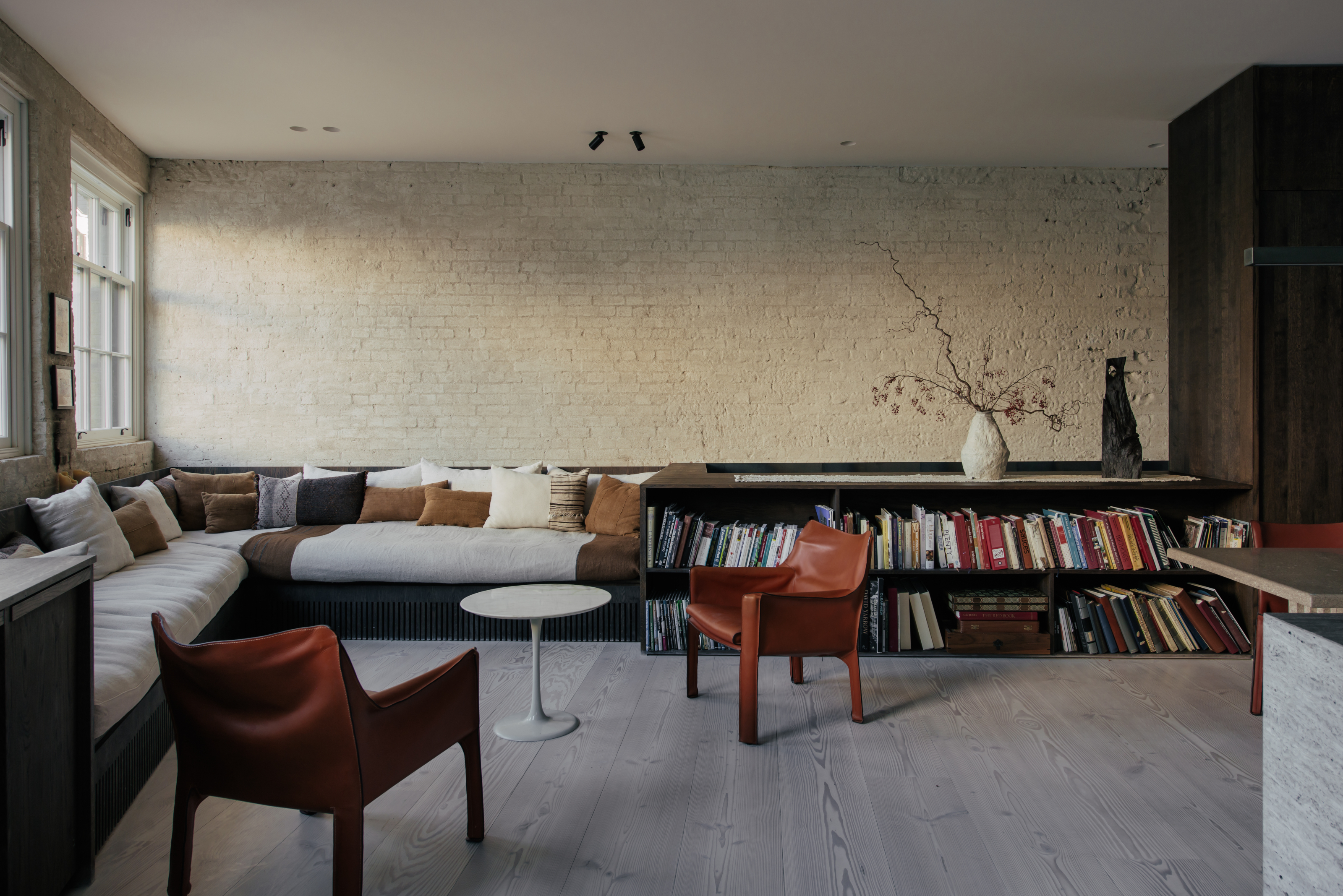 Living area with grey floors, cream brick walls, and built-in low bookshelf flowing into corner sofa