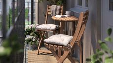 IKEA wooden outdoor wall table and chairs styled with cream cushions atop of a small balcony