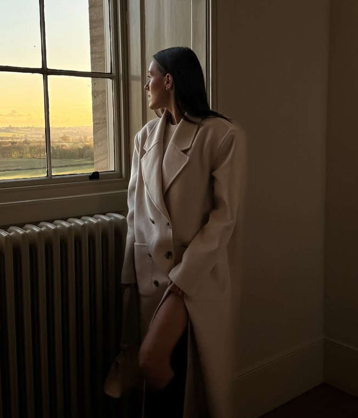 Emma Leger wears an oversized wool coat while watching the sunset over the British countryside