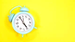 How to wake up early and not feel tired: A light blue alarm clock on a yellow background