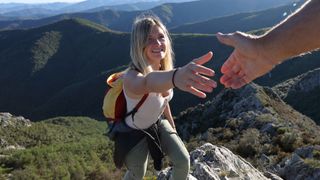 A hiker reaches out a hand to be helped up a mountain by a guide