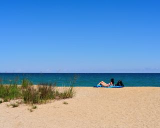 A lone woman relaxes in the sand among the dunes at Illinois Beach State Park at Zion, Illinois on the shore of Lake Michigan. USA.