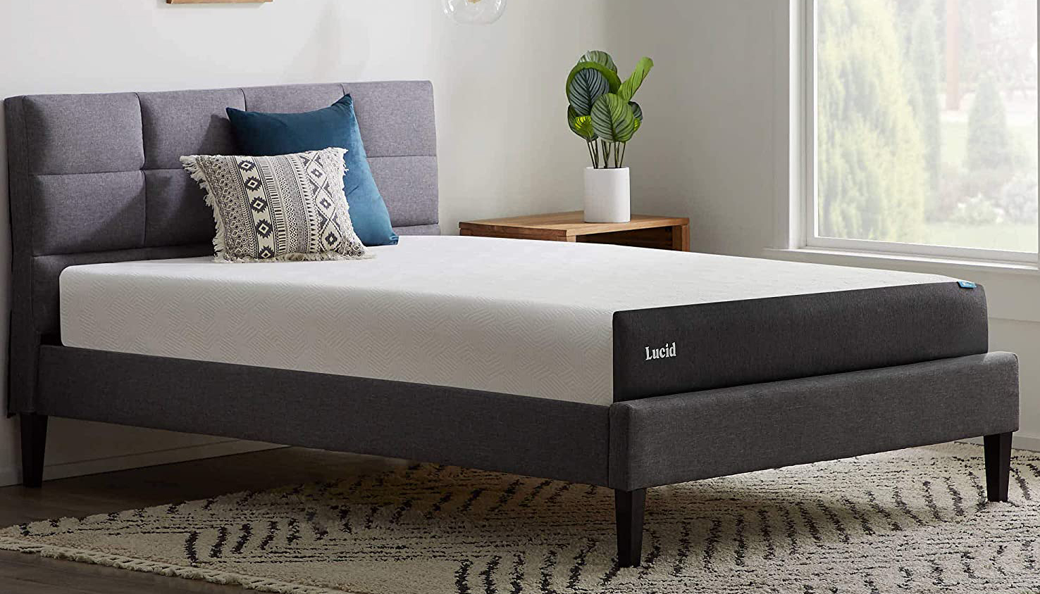Lucid full-size mattress on a bed frame with a padded headboard, near a window
