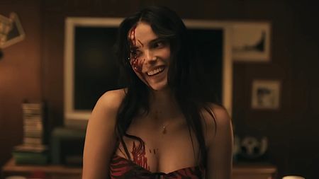 Inde Navarrette as Nikki laughs with blood on her face in Obsession.