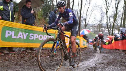  Nikki Brammeier is riding a cyclocross race in the mud with fans behind race course barriers 