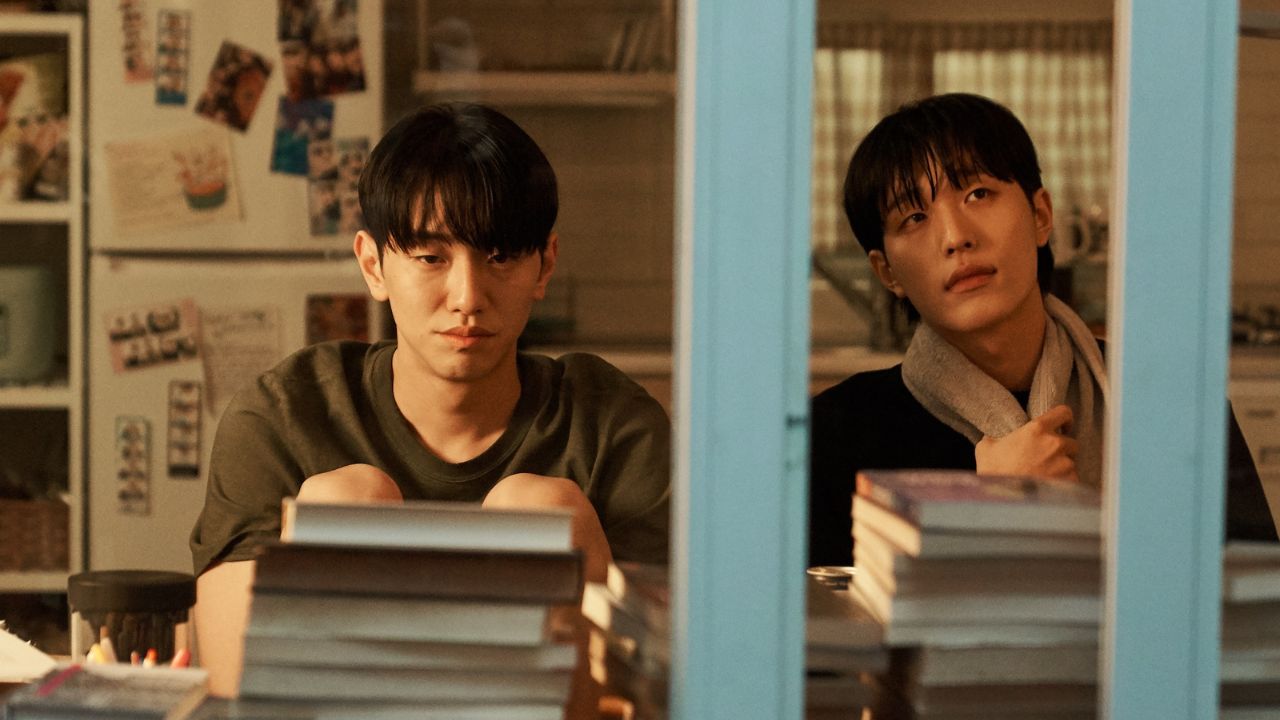 Two men sit in an apartment with books in front of them, in &#039;Love in the Big City.&#039;