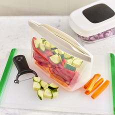 Silicone reusuable bag filled with chopped veg on chopping board next to potato peeler