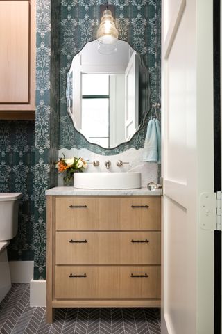 small bathroom with wallpaper, grey floor tiles, wooden vanity, marble top, mirror