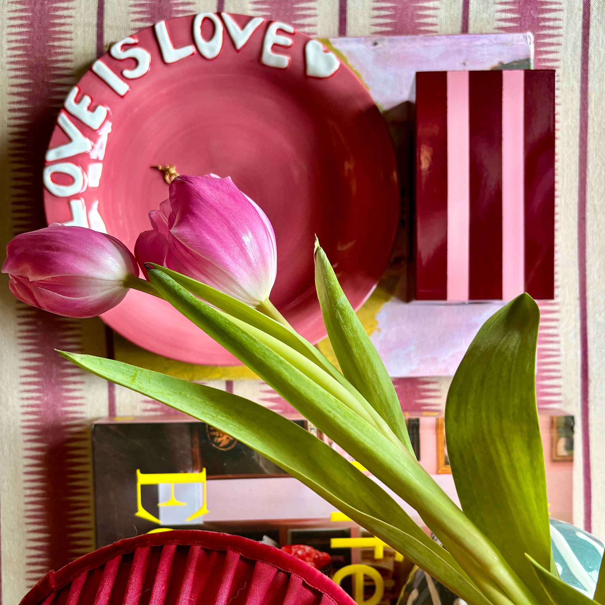 Dark pink plate, striped box, pink tulip and coffee table book placed on red and white striped fabric surface