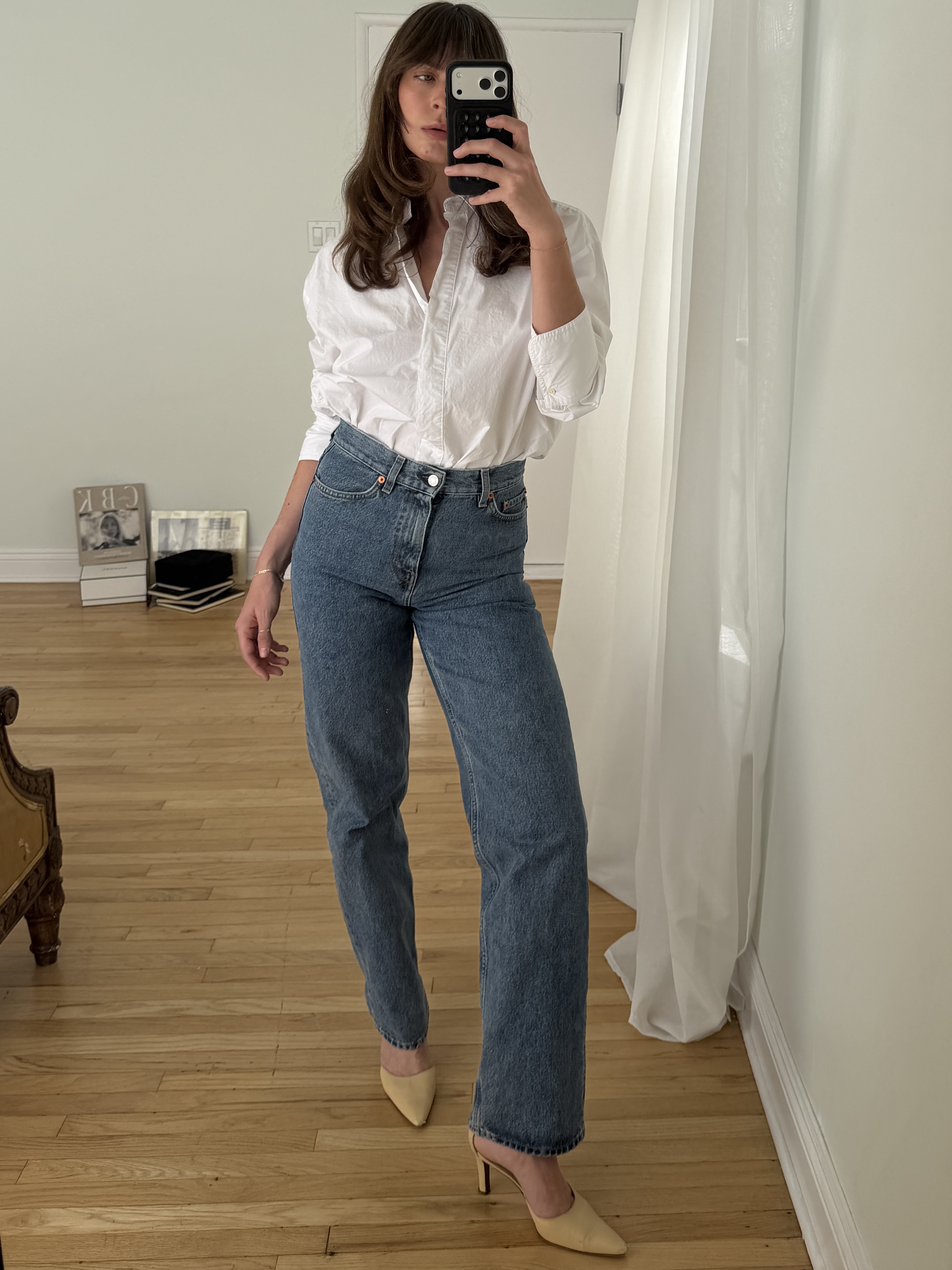 Kathryn Zahorak posing in mirror wearing white button-down shirt, jeans, and heels 