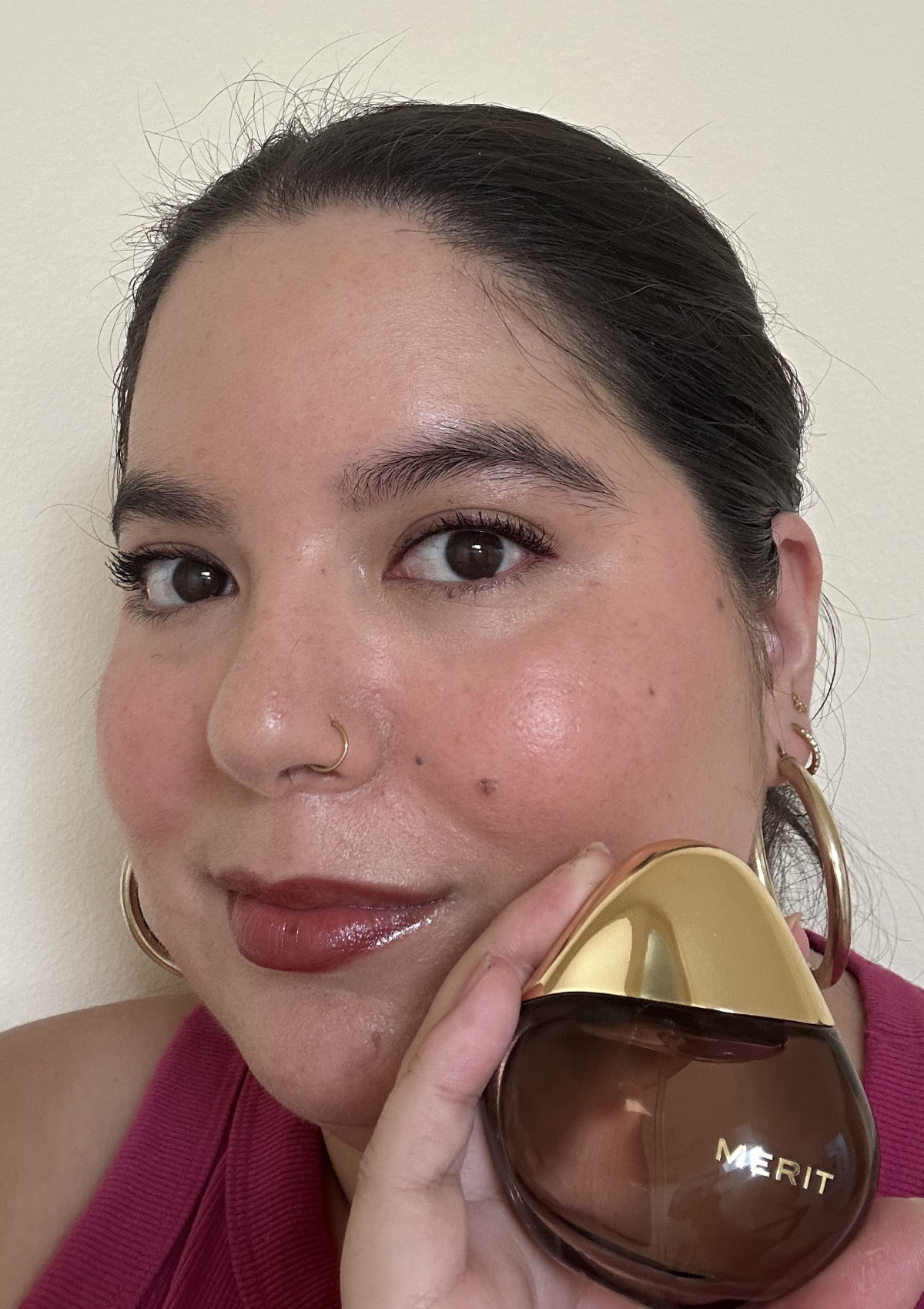 holding a Merit perfume bottle up to my cheek, gold cap, brown glass, glossy lips and rosy cheeks