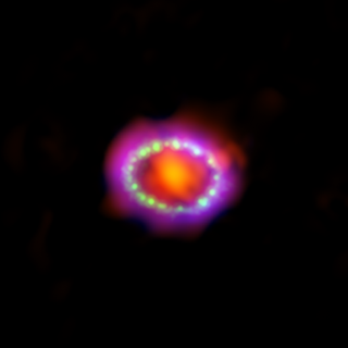 Against a black background, an orange/red blurry orb hangs in the center of a beaded ring of green, surrounded by pink and reddish gas.
