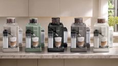 Image of five De'Longhi Rivelia coffee machines in different colors on a marble countertop in a beige kitchen.