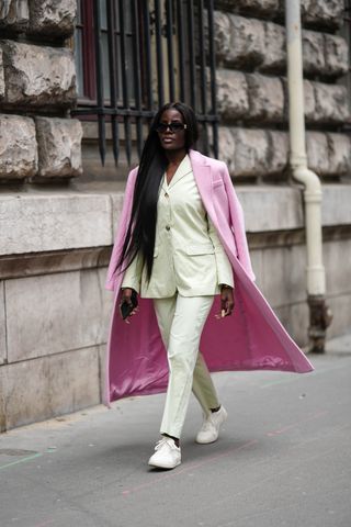 A guest wears black sunglasses from Versace, a white latte blazer jacket, matching white latte suit pants, a pale pink wool long coat, black socks, white leather sneakers , outside Hermes, during Paris Fashion Week - Womenswear Fall Winter 2023 2024, on March 04, 2023 in Paris, France.