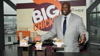 shaquille o'neal spreading his hands with a smile, beside a table with three chicken sandwiches