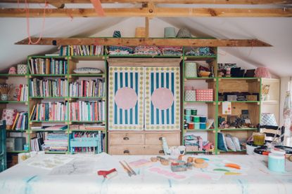 craft/sewing room with large table, books, shelving, cabinet, printing blocks, lampshades