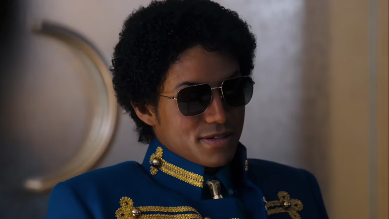 Jafaar Jackson as Michael Jackson, wearing sunglass and blue military-style top