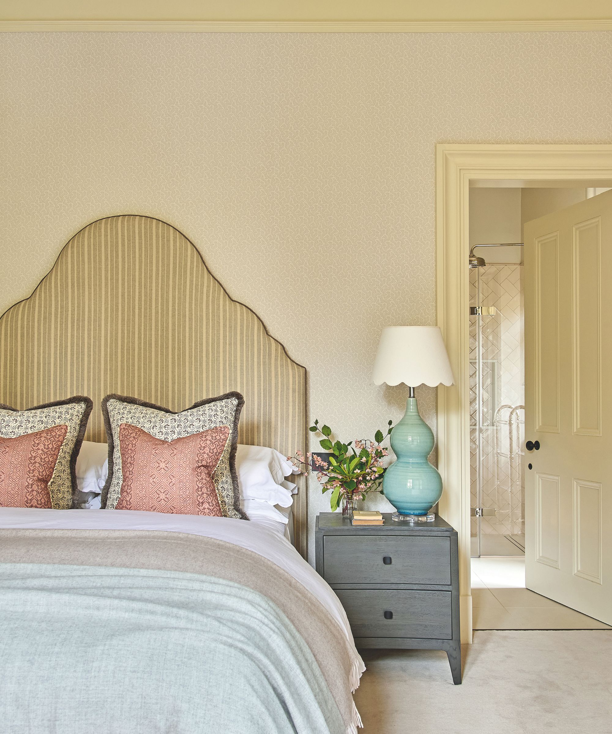 Pale yellow bedroom with large striped headboard, gray bedside table and blue lamp