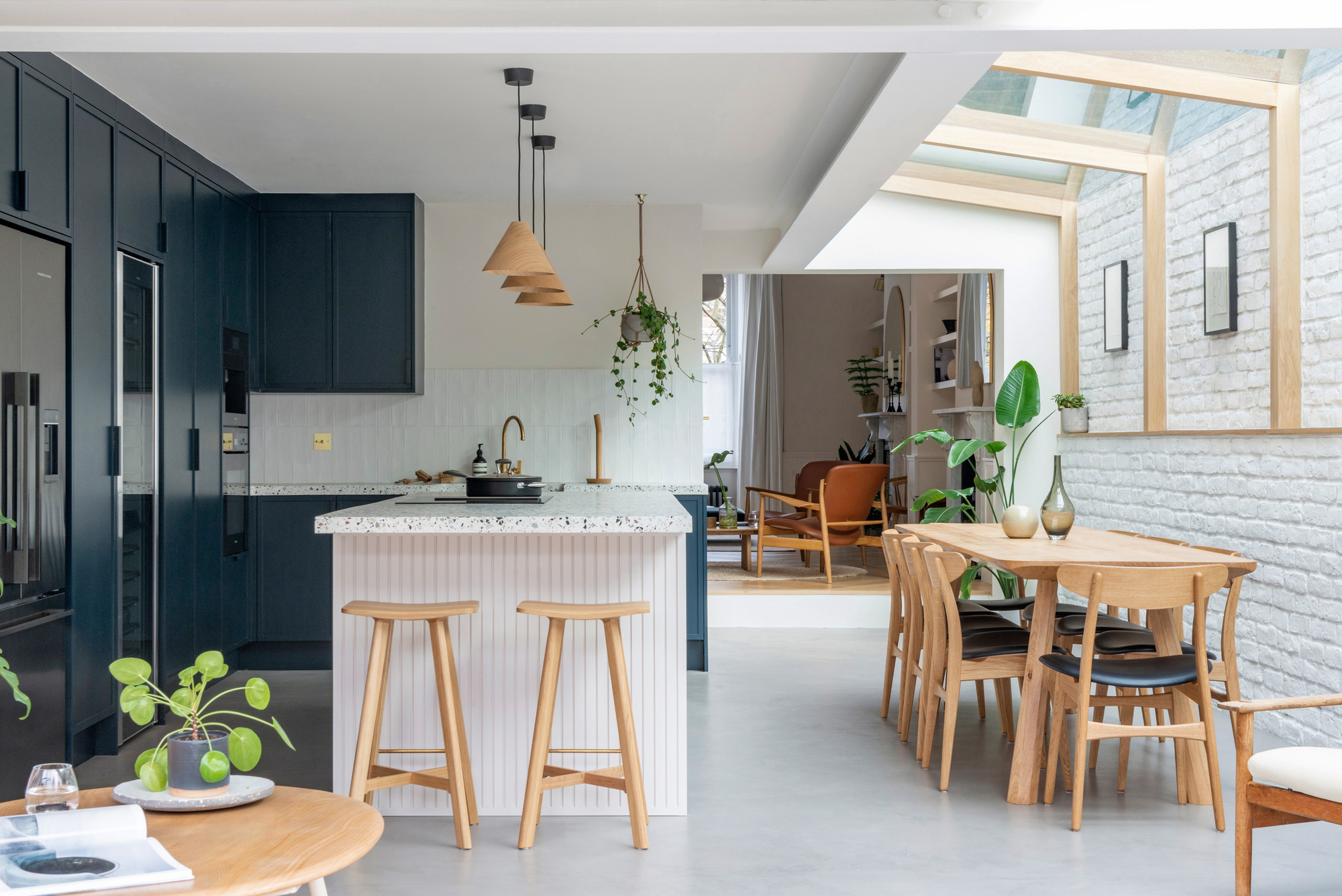 modern home with open plan kitchen, polished concrete floor, skylights over dining table, with dark kitchen cabinetry and fluted white kitchen island with terrazzo counter and timber bar stools