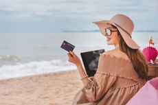 Person holds credit card as they sit on the beach.