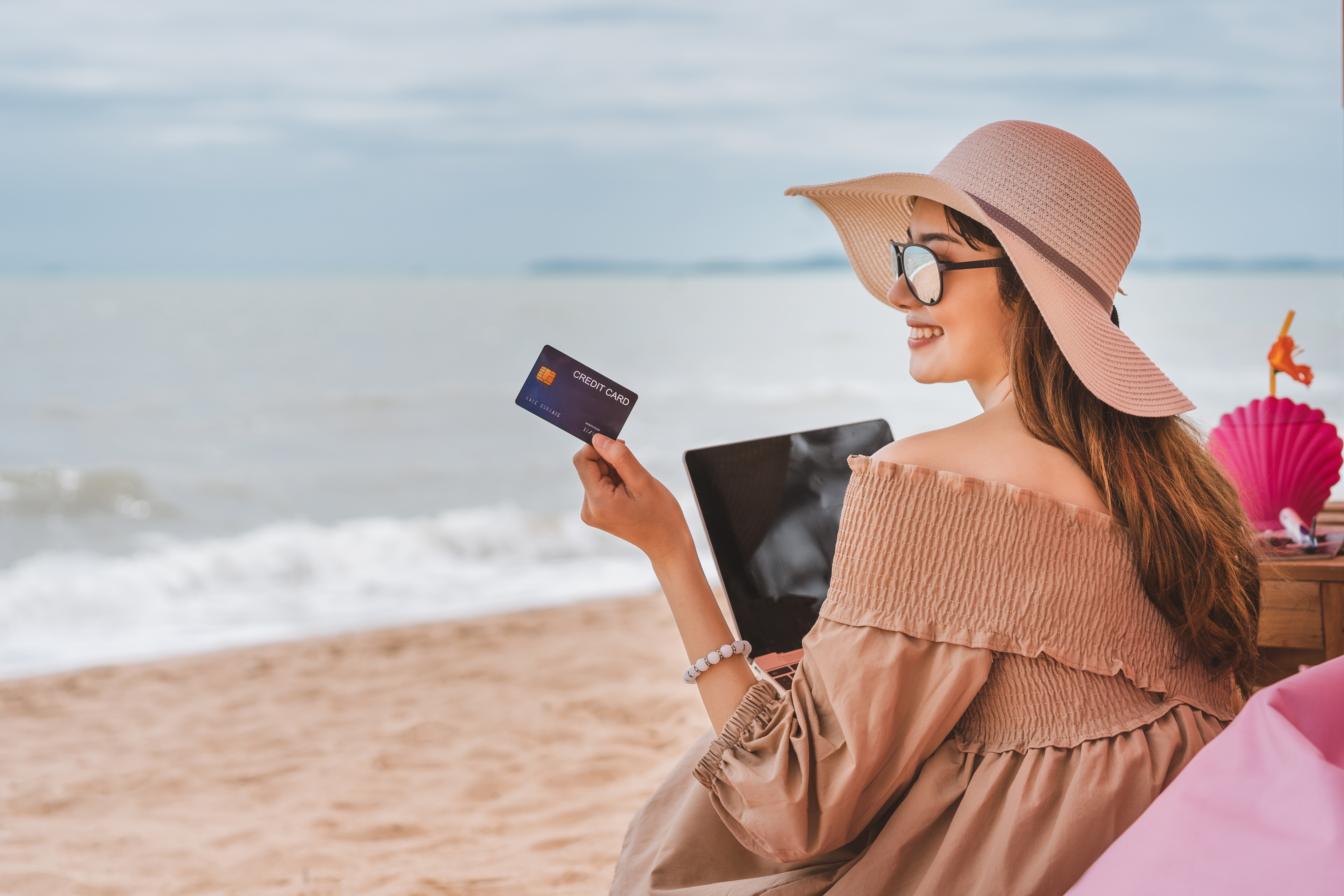 Person holds credit card as they sit on the beach.