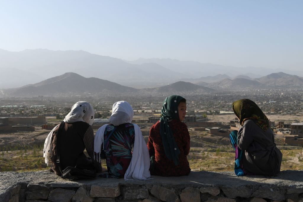 Afghan girls sit while looking out from a hilltop overlooking Kabul