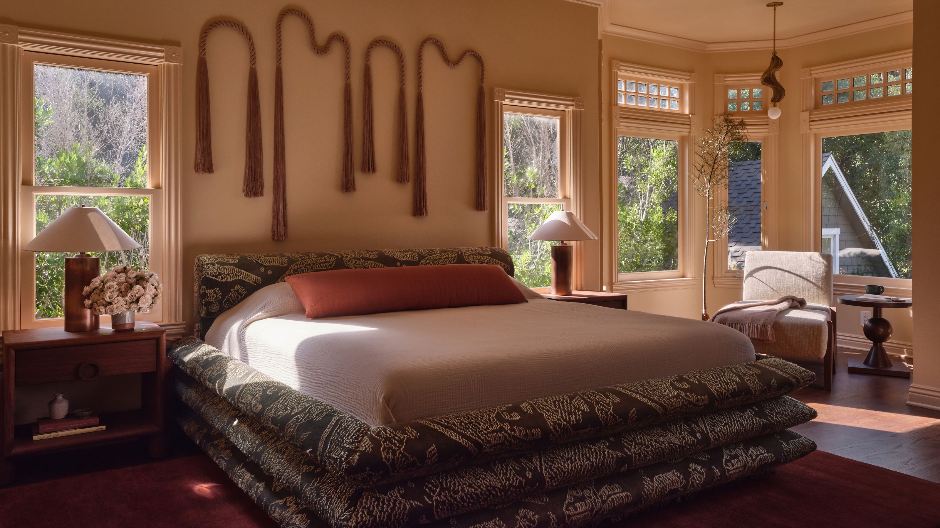 a warm dusky bedroom with original timber bay window, modern patterned bed and unique fringed wall art